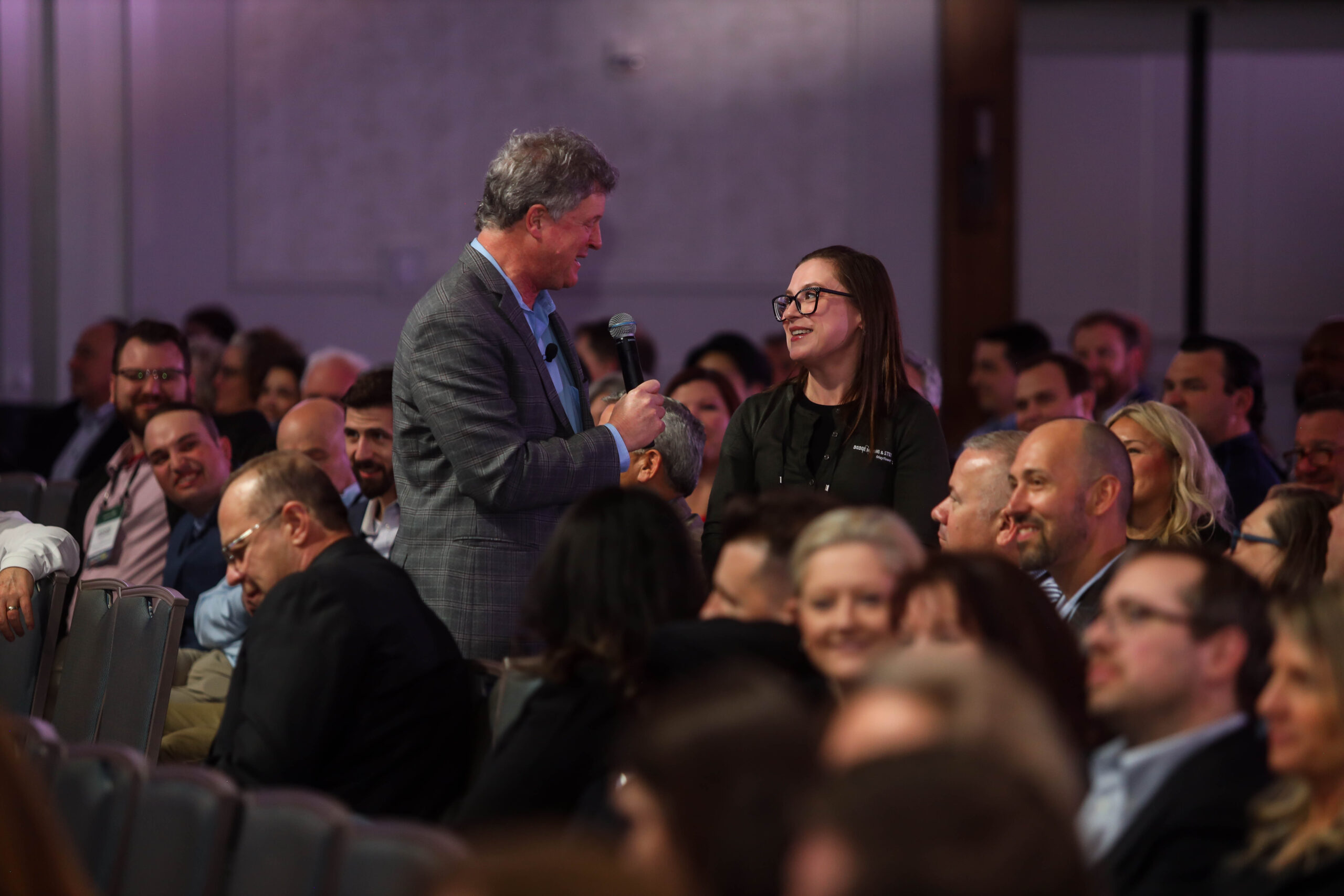 Greg Schwem interacting with a smiling audience member during a corporate keynote presentation, surrounded by engaged and laughing attendees in a conference setting.
